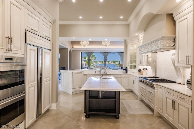 kitchen featuring a center island with sink, appliances with stainless steel finishes, tasteful backsplash, custom range hood, and sink