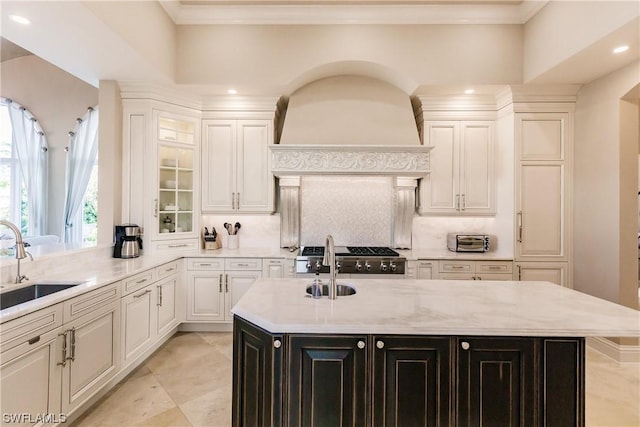 kitchen featuring an island with sink, stove, sink, light stone counters, and decorative backsplash