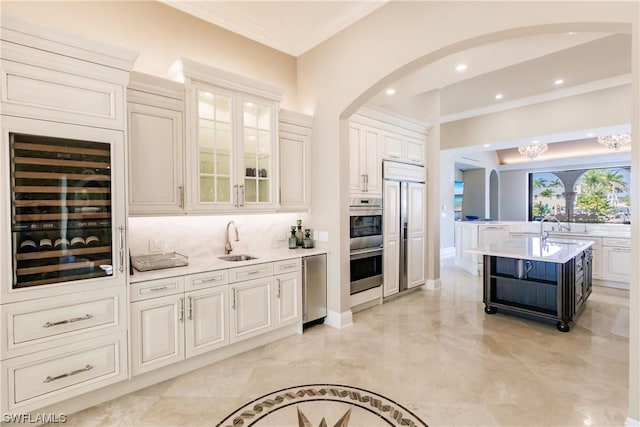 kitchen with a kitchen island with sink, stainless steel appliances, sink, beverage cooler, and crown molding