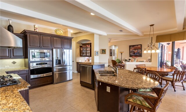 kitchen with dark brown cabinets, stainless steel appliances, beam ceiling, a breakfast bar area, and a kitchen island with sink