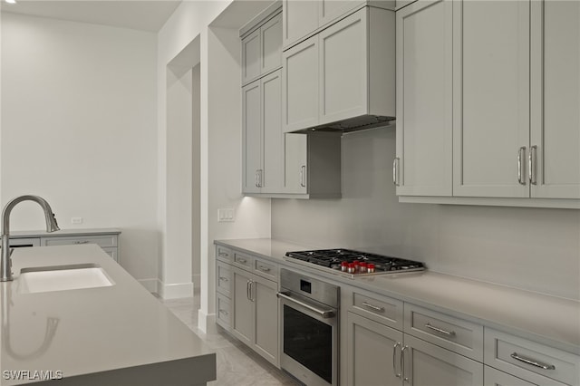 kitchen with stainless steel appliances, gray cabinets, sink, and wall chimney range hood