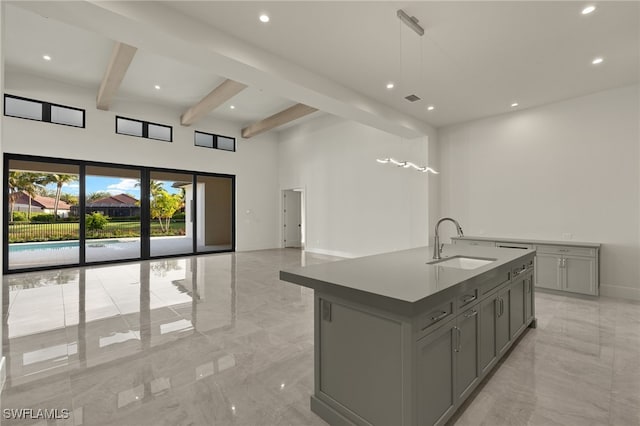 kitchen featuring sink, gray cabinets, a kitchen island with sink, beam ceiling, and decorative light fixtures