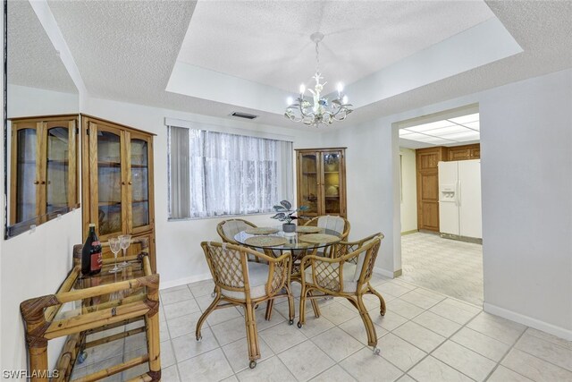 dining area featuring light tile patterned flooring, a textured ceiling, and a tray ceiling