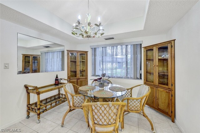 tiled dining area featuring a notable chandelier, a tray ceiling, and a textured ceiling