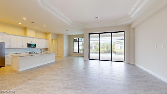 kitchen with a center island with sink, a raised ceiling, white cabinetry, and appliances with stainless steel finishes