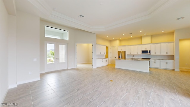 kitchen with a kitchen island with sink, french doors, sink, white cabinetry, and stainless steel appliances