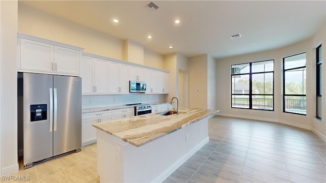 kitchen with white cabinetry, light stone countertops, stainless steel appliances, decorative backsplash, and a kitchen island with sink