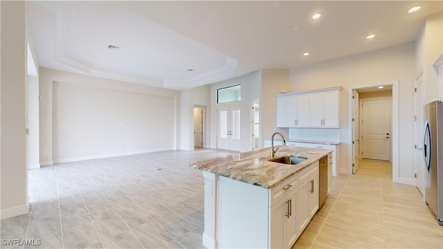 kitchen featuring light stone countertops, sink, a raised ceiling, a center island with sink, and white cabinets