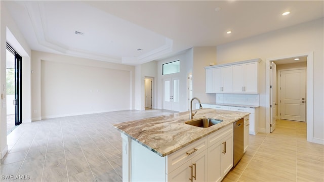 kitchen with light stone countertops, a raised ceiling, a kitchen island with sink, sink, and white cabinetry