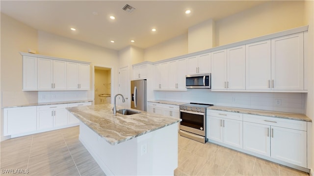 kitchen with sink, light stone countertops, an island with sink, appliances with stainless steel finishes, and white cabinetry