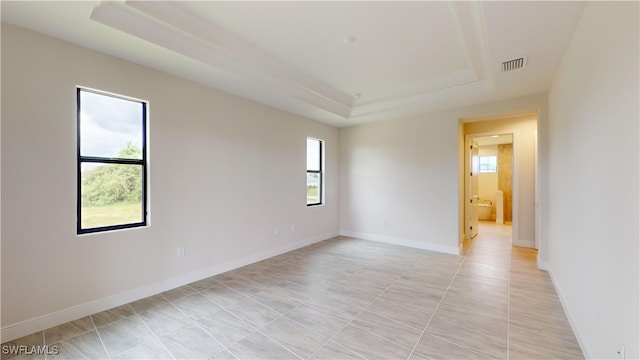 tiled empty room featuring a raised ceiling and a wealth of natural light