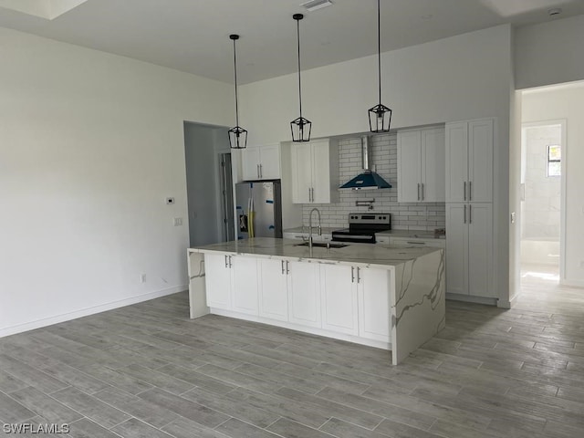 kitchen with pendant lighting, light stone countertops, wall chimney exhaust hood, appliances with stainless steel finishes, and white cabinetry