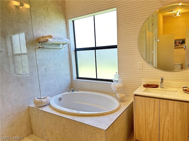 bathroom with a healthy amount of sunlight, vanity with extensive cabinet space, and tiled tub