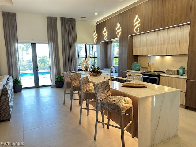 kitchen with sink, light tile flooring, an island with sink, stainless steel range, and light stone countertops