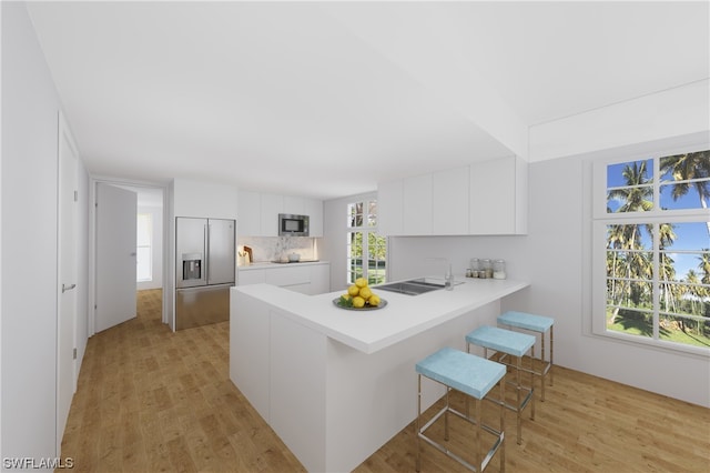 kitchen featuring built in appliances, a kitchen breakfast bar, white cabinets, light hardwood / wood-style flooring, and backsplash