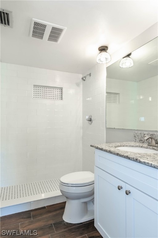 bathroom with a tile shower, large vanity, toilet, and wood-type flooring