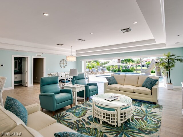 living room featuring a chandelier, a raised ceiling, and light wood-type flooring