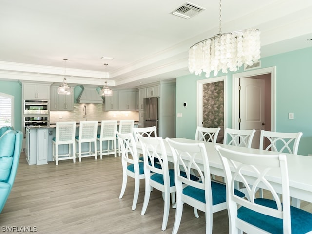 dining area featuring a chandelier, light hardwood / wood-style floors, a tray ceiling, and sink