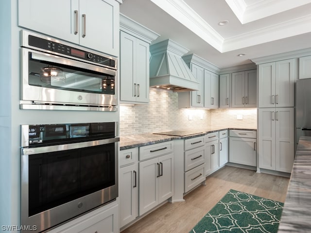 kitchen with ornamental molding, light stone countertops, custom exhaust hood, tasteful backsplash, and light wood-type flooring