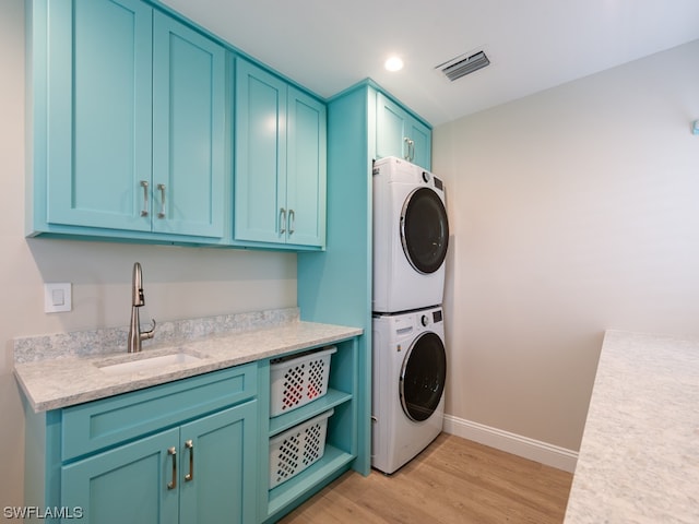 laundry room with cabinets, stacked washing maching and dryer, sink, and light wood-type flooring