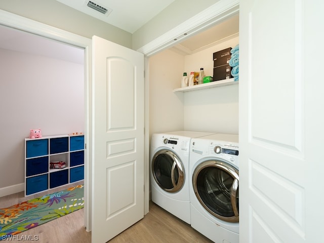 laundry room with washing machine and clothes dryer and light hardwood / wood-style floors