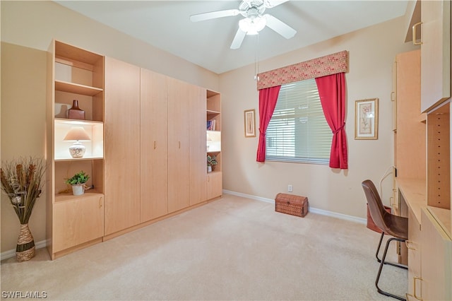 carpeted office space with built in shelves and ceiling fan