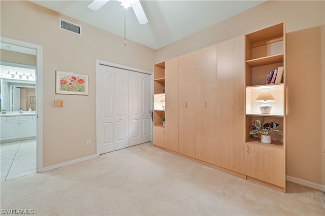 unfurnished bedroom with ceiling fan, light colored carpet, ensuite bathroom, and a closet