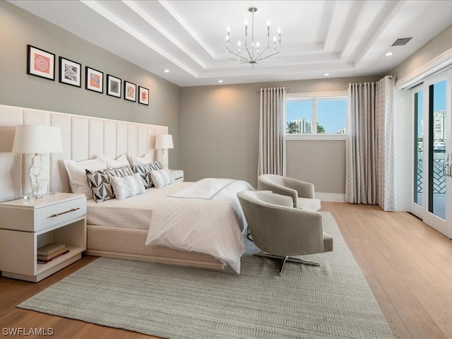 bedroom with a tray ceiling, access to exterior, light hardwood / wood-style flooring, and a notable chandelier