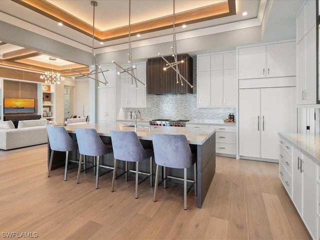 kitchen with white cabinetry, a notable chandelier, a tray ceiling, and sink