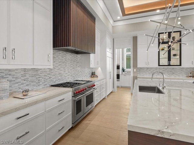 kitchen featuring white cabinetry, sink, range with two ovens, light stone counters, and wall chimney range hood