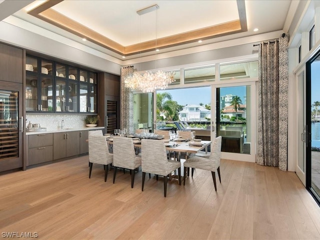 dining area featuring an inviting chandelier, a tray ceiling, light hardwood / wood-style flooring, and indoor wet bar