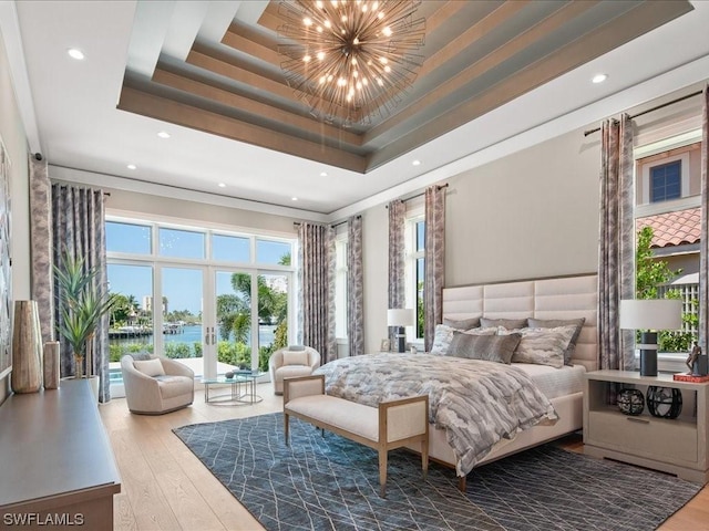 bedroom featuring a notable chandelier, a tray ceiling, hardwood / wood-style flooring, and a water view