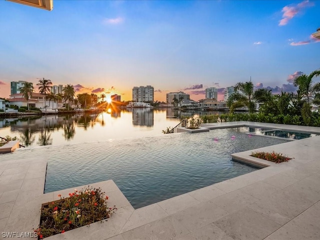 pool at dusk featuring a patio and a water view