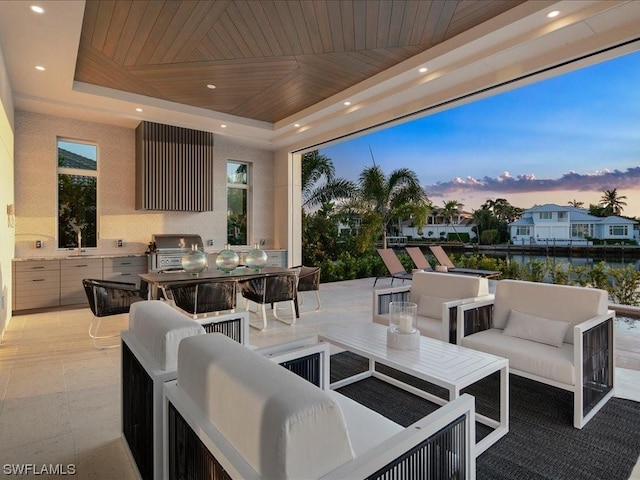 patio terrace at dusk with a grill, an outdoor hangout area, exterior kitchen, and a water view