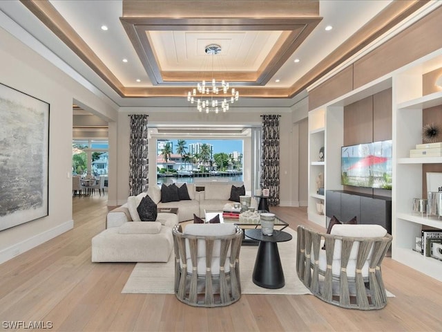 living room featuring built in shelves, a raised ceiling, an inviting chandelier, and light wood-type flooring