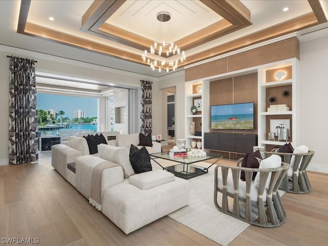 living room with built in shelves, light hardwood / wood-style flooring, a raised ceiling, and a chandelier