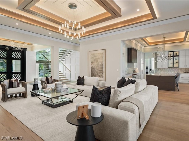 living room featuring a tray ceiling, a chandelier, sink, and light wood-type flooring