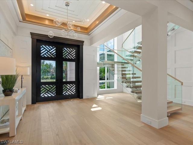 foyer entrance with crown molding, an inviting chandelier, a tray ceiling, french doors, and light wood-type flooring