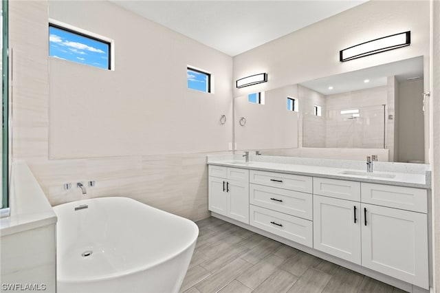 bathroom featuring tile walls, double vanity, a stall shower, a sink, and a freestanding tub