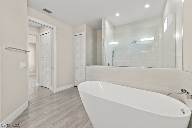 bathroom featuring wood finish floors, a closet, visible vents, a freestanding bath, and a shower stall