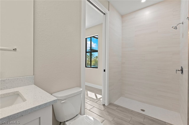 full bathroom with toilet, a tile shower, and vanity