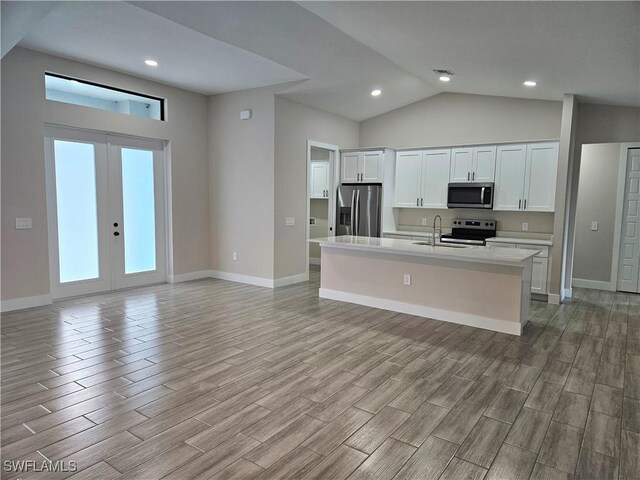 kitchen with a kitchen island with sink, white cabinetry, light countertops, french doors, and appliances with stainless steel finishes