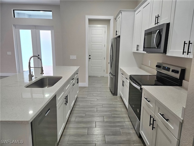 kitchen with light stone countertops, wood tiled floor, stainless steel appliances, white cabinetry, and a sink