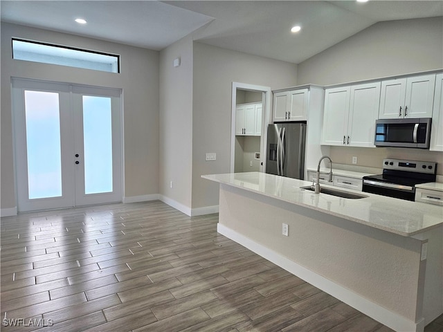 kitchen with stainless steel appliances, a sink, white cabinets, light wood-type flooring, and light stone countertops