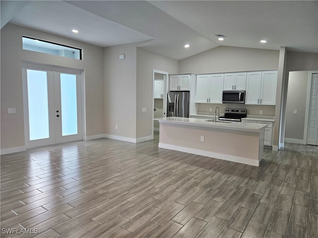 kitchen with an island with sink, stainless steel appliances, white cabinets, and light hardwood / wood-style floors