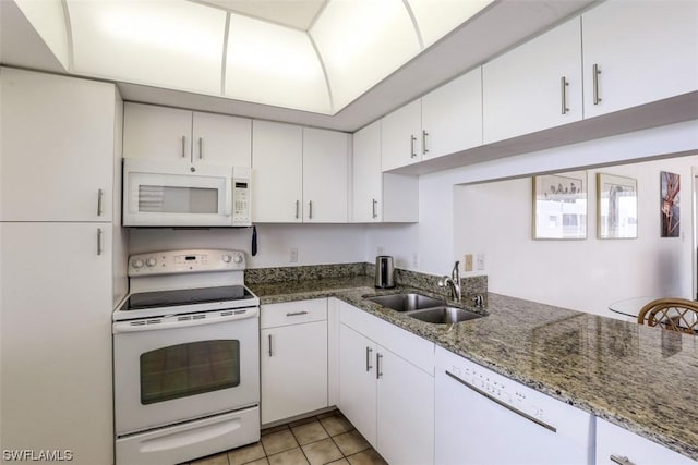 kitchen with dark stone counters, light tile patterned flooring, white appliances, white cabinetry, and a sink