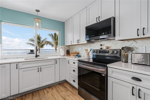 kitchen featuring light hardwood / wood-style floors, stainless steel appliances, decorative light fixtures, white cabinetry, and backsplash