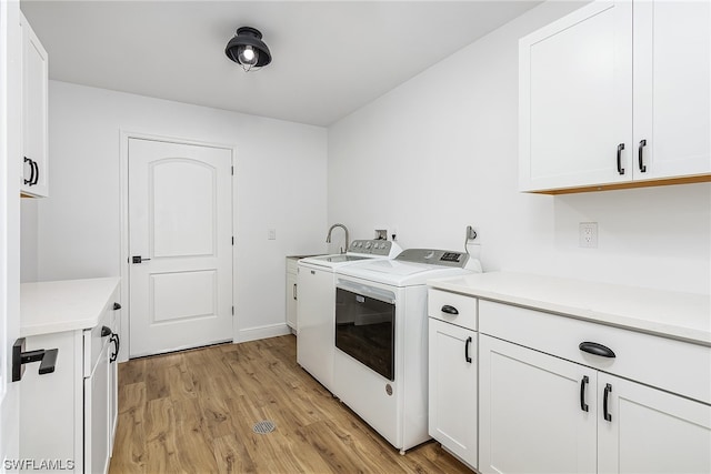 laundry area featuring independent washer and dryer, light hardwood / wood-style flooring, and cabinets