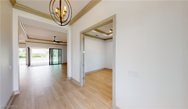 hall with a chandelier, a tray ceiling, ornamental molding, and light wood-type flooring