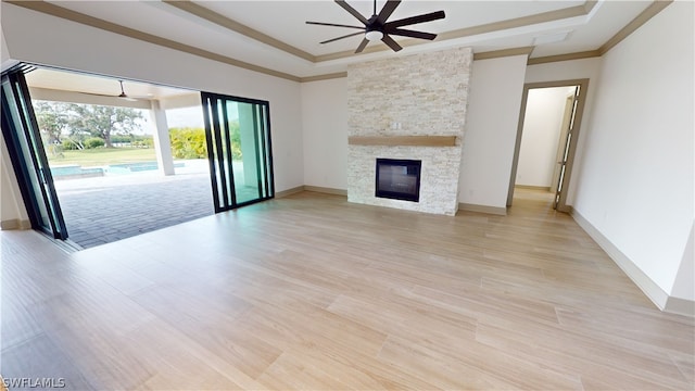 unfurnished living room featuring light hardwood / wood-style flooring, ceiling fan, a tray ceiling, and a stone fireplace